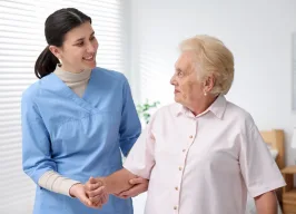 Pflegekraft in Arbeitskleidung hält die Hand einer älteren Dame und unterhält sich mit ihr